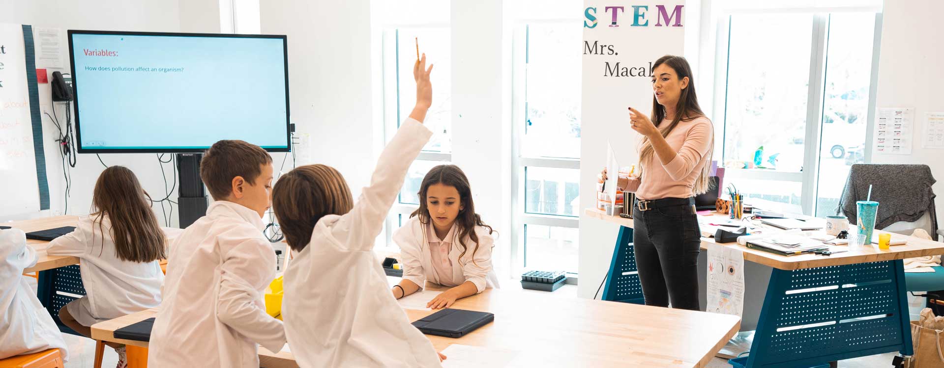 Child raising hand with teach in STEM class