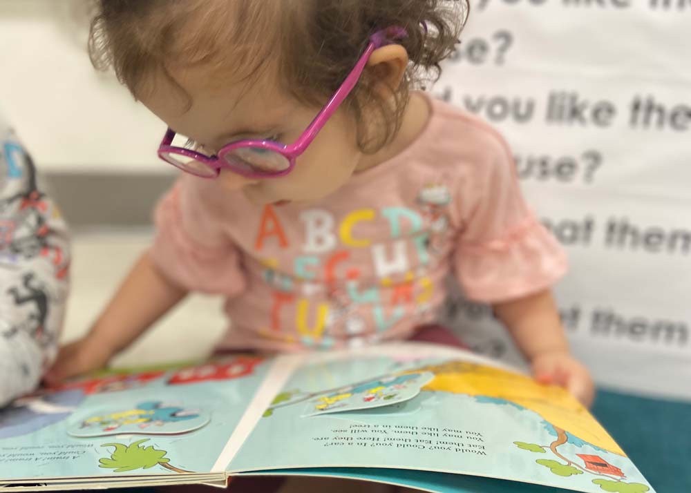 young toddler with glasses reading a book
