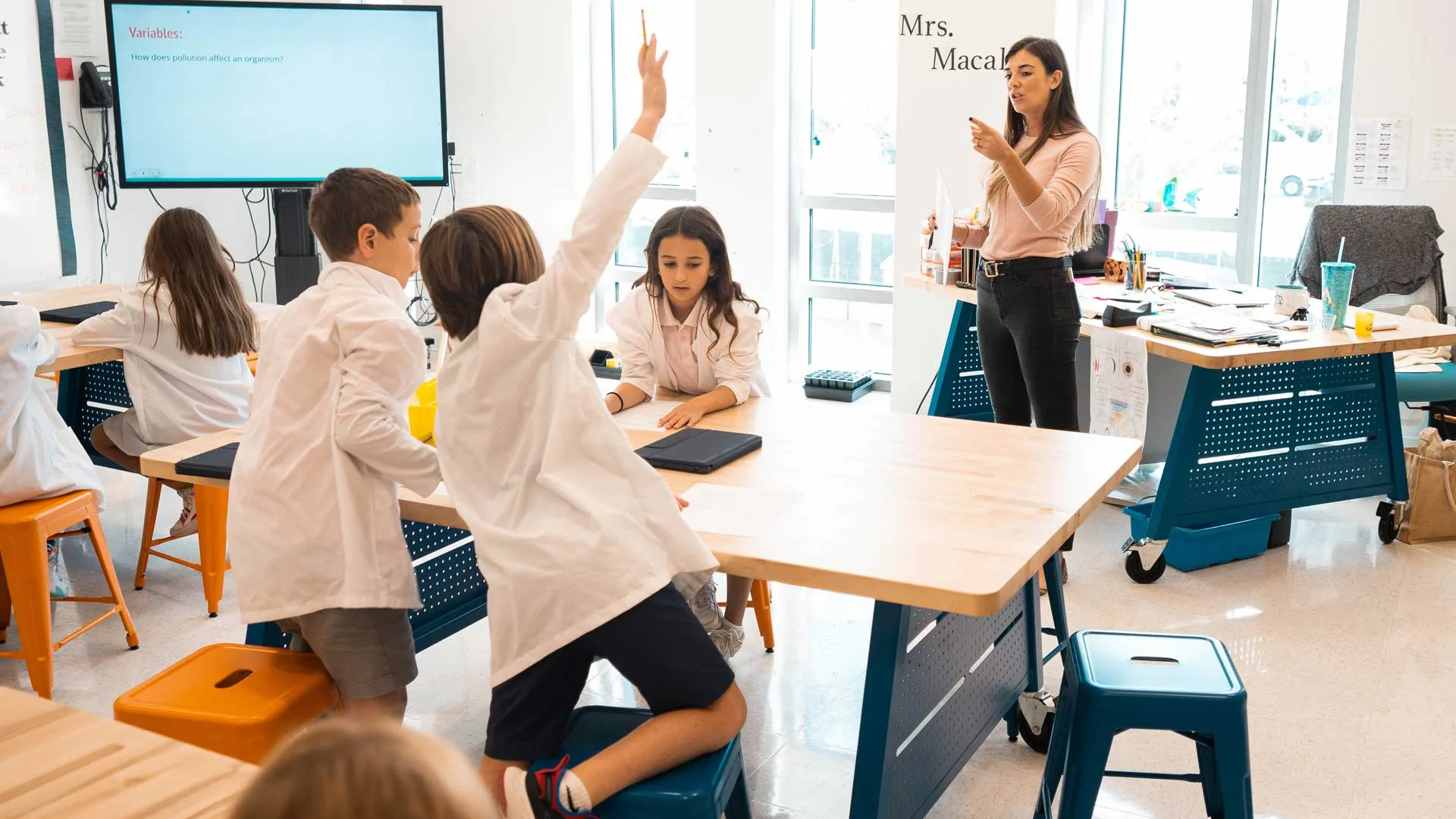 student raises hand while teacher stands and teaches